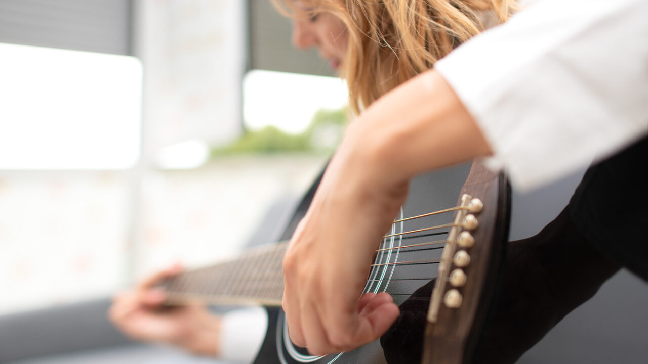 Close-up of a left-handed musician strumming a black acoustic guitar