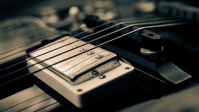 Macro shot of electric guitar humbucker pickup with metal cover and guitar strings in sharp focus