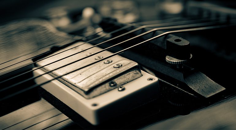 Macro shot of electric guitar humbucker pickup with metal cover and guitar strings in sharp focus