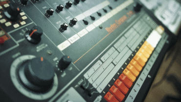 808 day: Close-up view of Roland TR-808 drum machine featuring colorful step-sequencer buttons and analog controls.