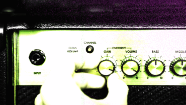 Close-up of a guitar amp with gain and volume knobs being adjusted, representing overdrive pedal history